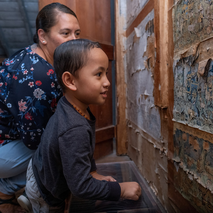 Mother and son crouching down to look at historic wallpaper in the attic