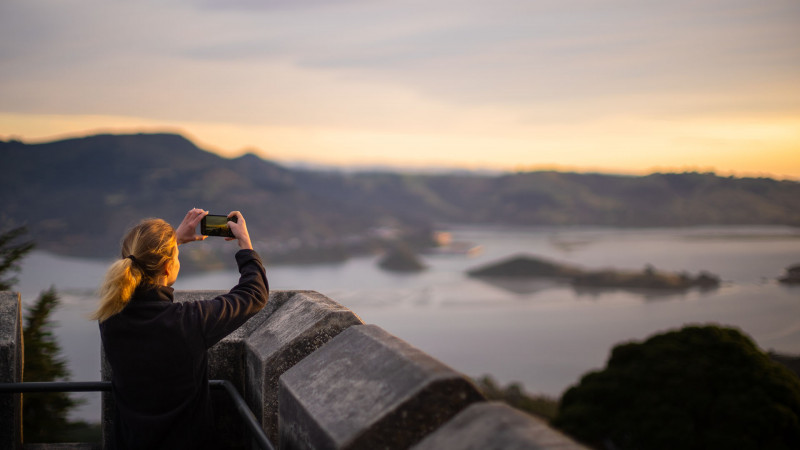 A woman takes a photo of the view from the top of Larnach Castle over the harbour