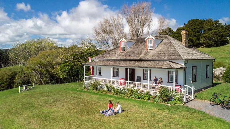 Māngungu Mission with a couple picnicking on the lawn and a couple standing on the veranda