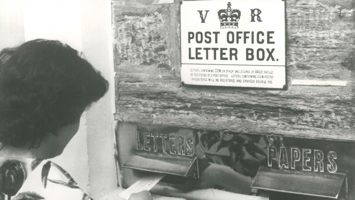 Historic black and white photo showing Mrs J Shepherd of Alexandra posts envelope through mail slots at Ophir Post Office in 1961