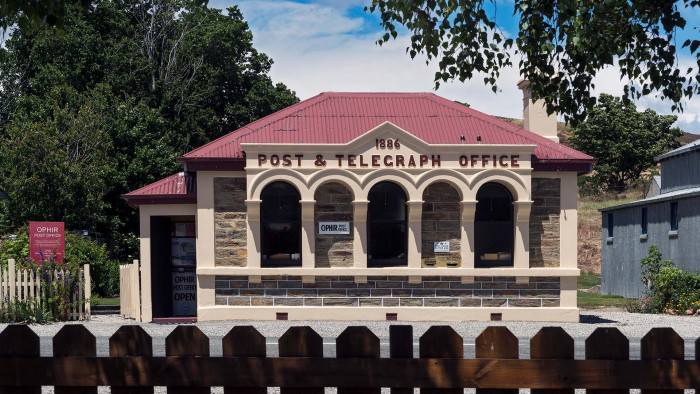 Straight on photo of Ophir Post office building with the top of a picket fence taken from across the street
