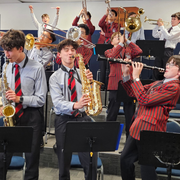 Eleven teenage boys in grey, red striped uniforms enthusiastically play various brass instruments.