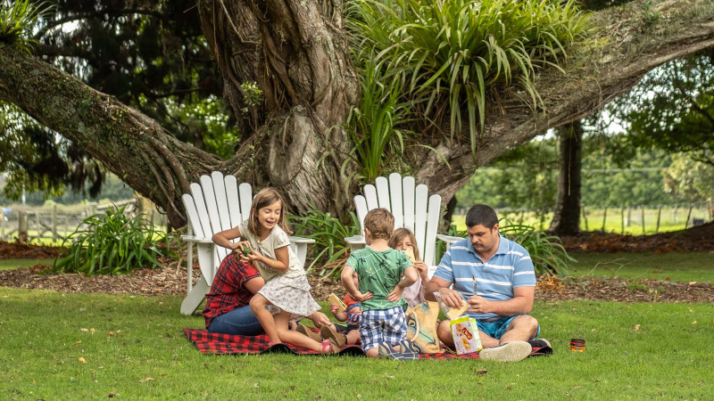 A family picnicking on the lawn under the tress in the mission grounds
