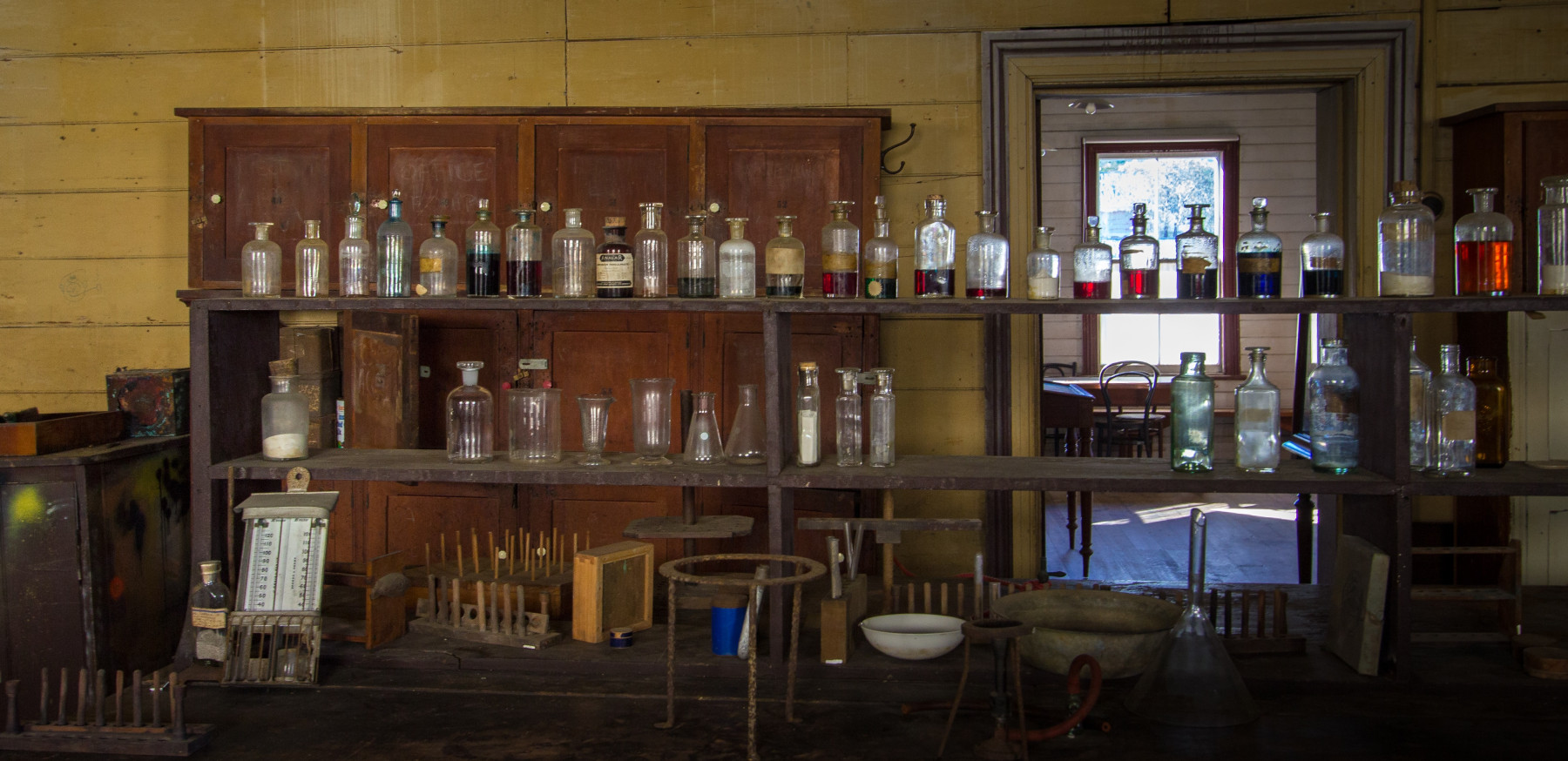 Historic chemical bottles on a shelf with a doorway behind.