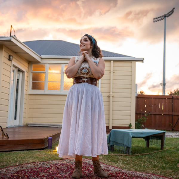 Young woman on a backyard lawn in white clasps hands and looks to sky.
