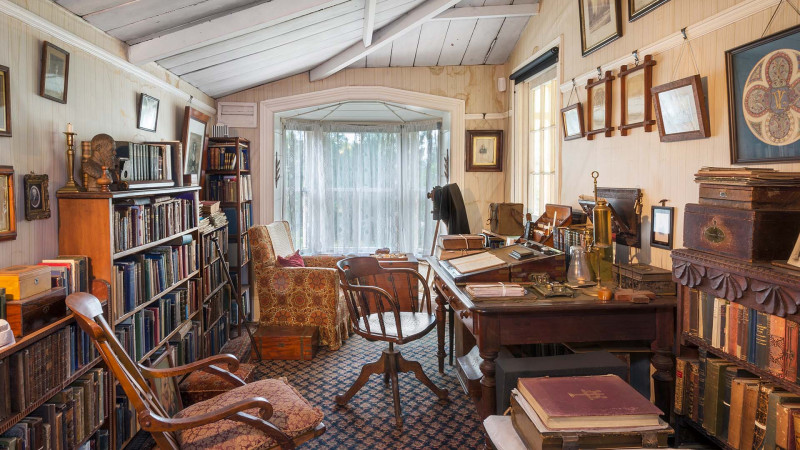 The study at Ewelme Cottage filled with books, photographs, a desk and chair, as well as two more chairs for guests