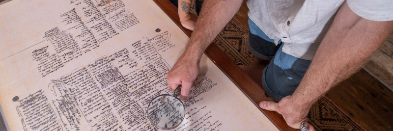 Two people using a magnifying glass to look at a copy of the Treaty of Waitangi