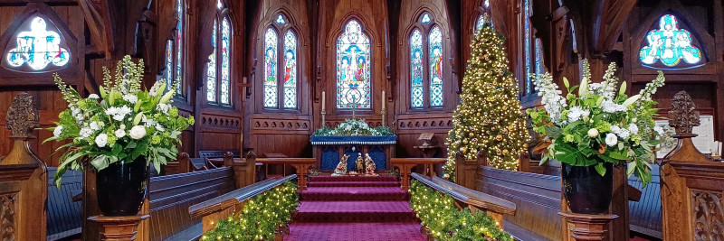 Christmas tree and nativity scene at altar beneath stained glass windows. 